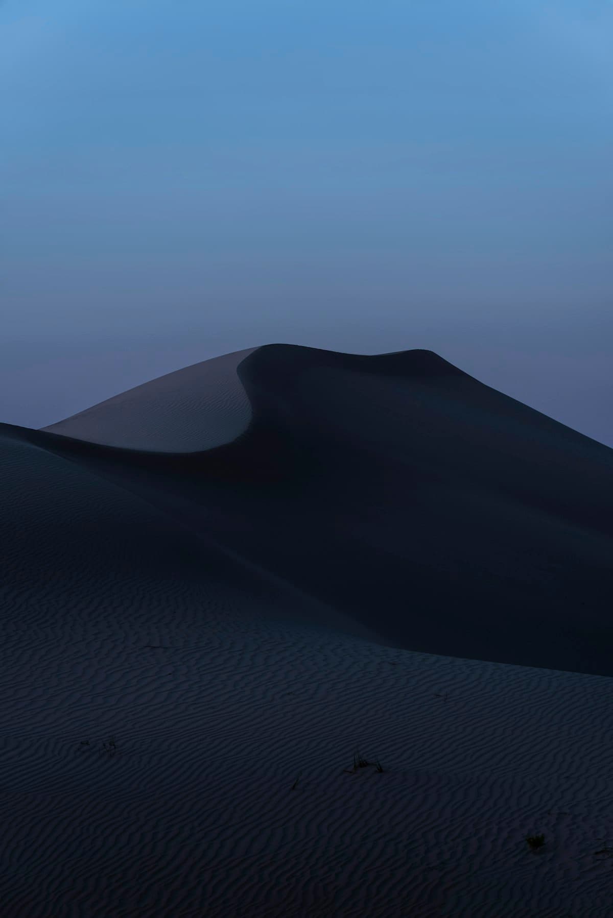 Towering desert sand dunes at dusk, sculpted into deep shadow and warm low light