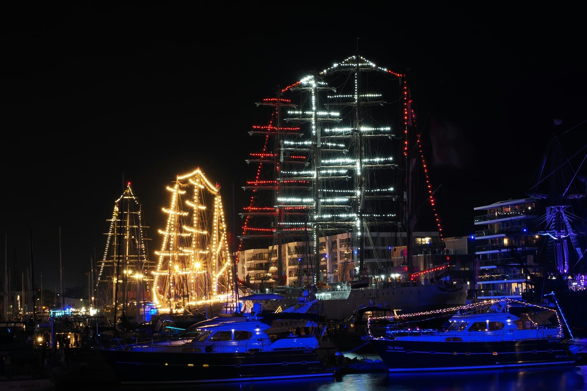 A harbor at night with illuminated tall ships reflecting on dark water