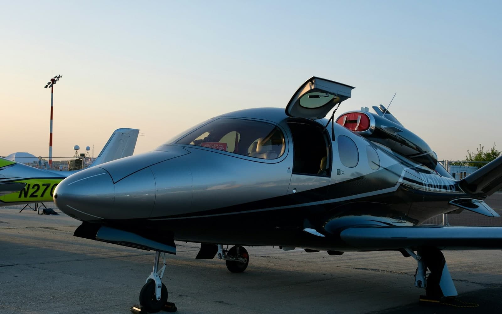 A sleek private jet parked on the tarmac with its cabin door open in low evening light