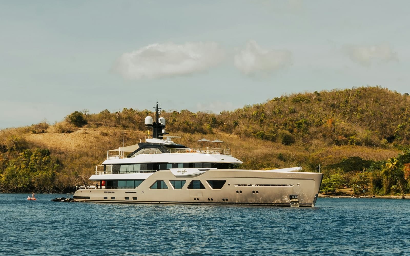 A large luxury yacht anchored off a quiet island coastline in clear blue water