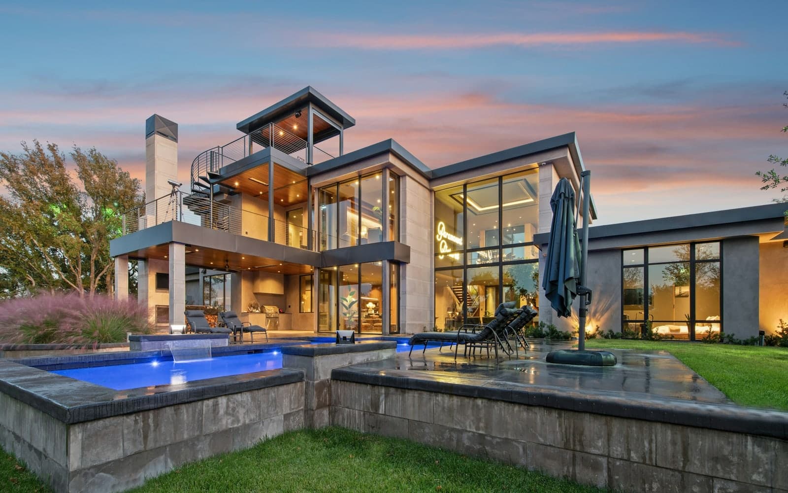 A modern luxury residence with glass walls, terraces, and a pool illuminated at dusk