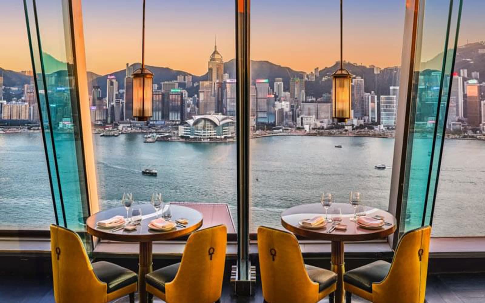 A private dining table set beside floor-to-ceiling windows overlooking a city harbor